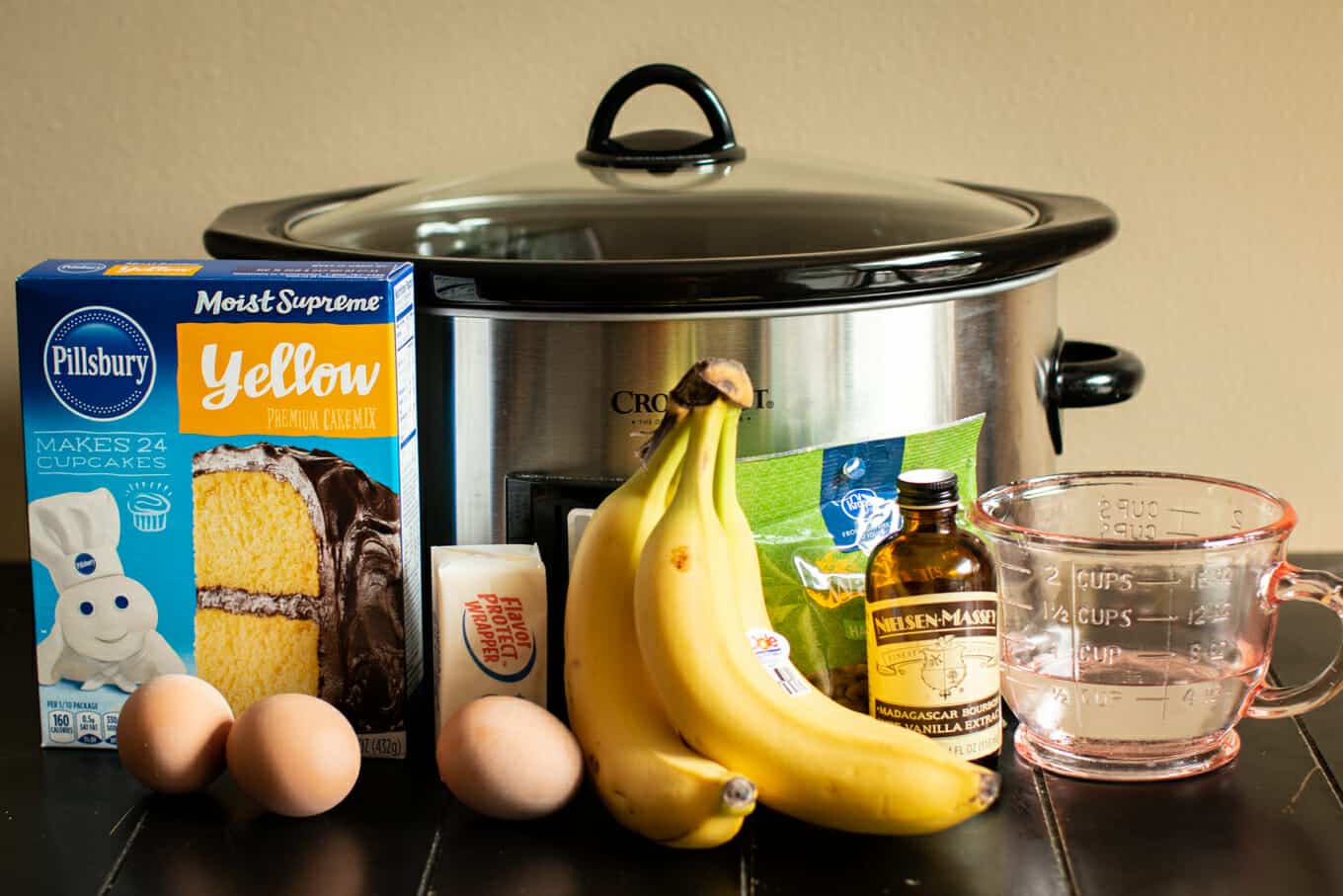 yellow cake, eggs, bananas, vanilla, butter, pecans, and water in front of slow coooker.