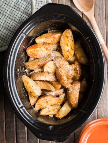 potato wedges in slow cooker with wooden spoon beside.