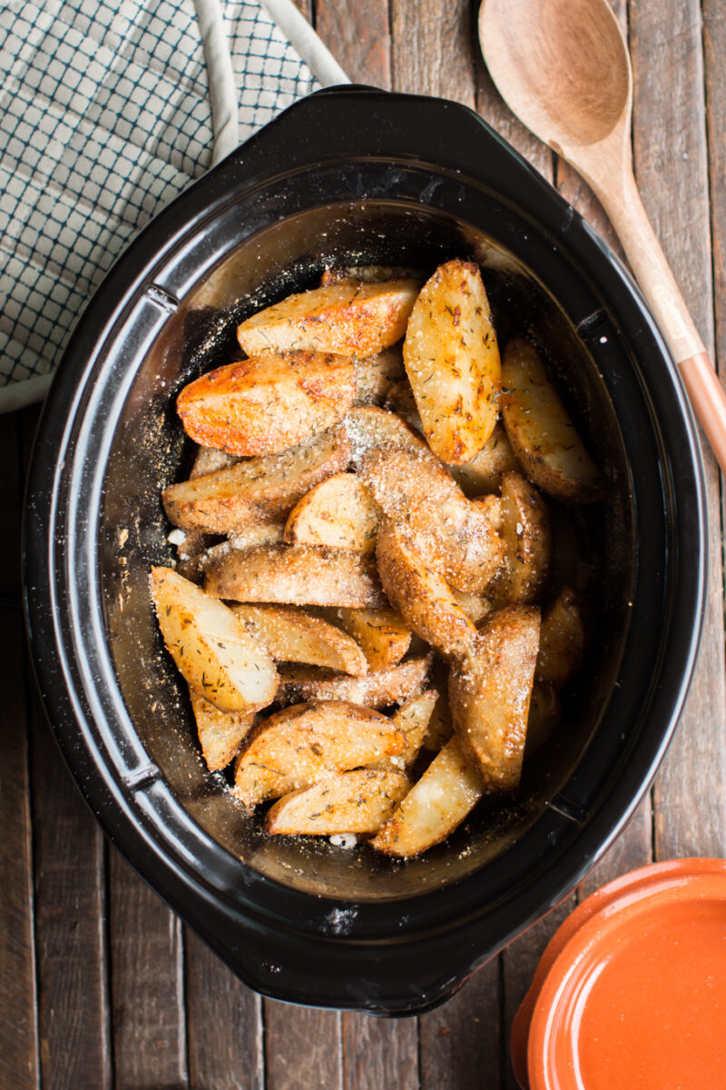 potato wedges in slow cooker with wooden spoon beside.