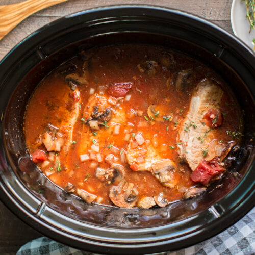 pork chop cacciatore in slow cooker with wooden spoon next to it.