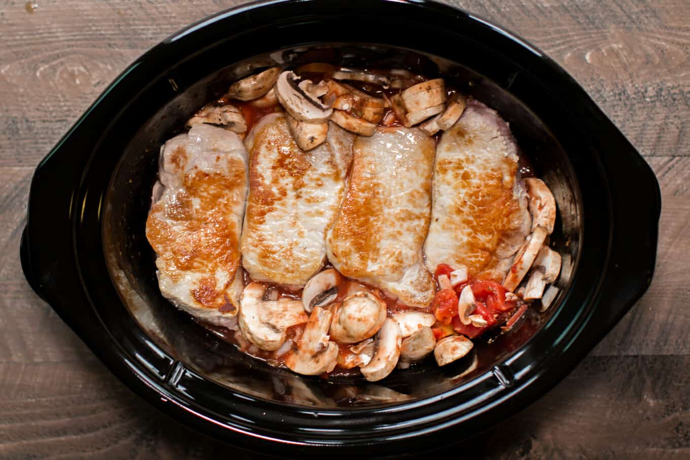 brown pork chops in slow cooker with mushrooms and tomatoes.