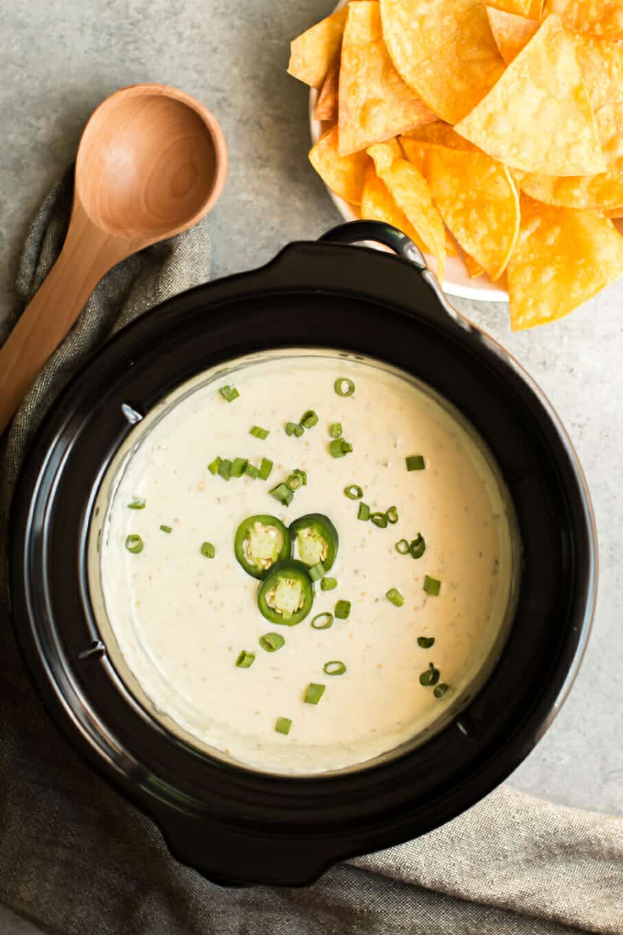 queso verde in slow cooker with chips on the side.