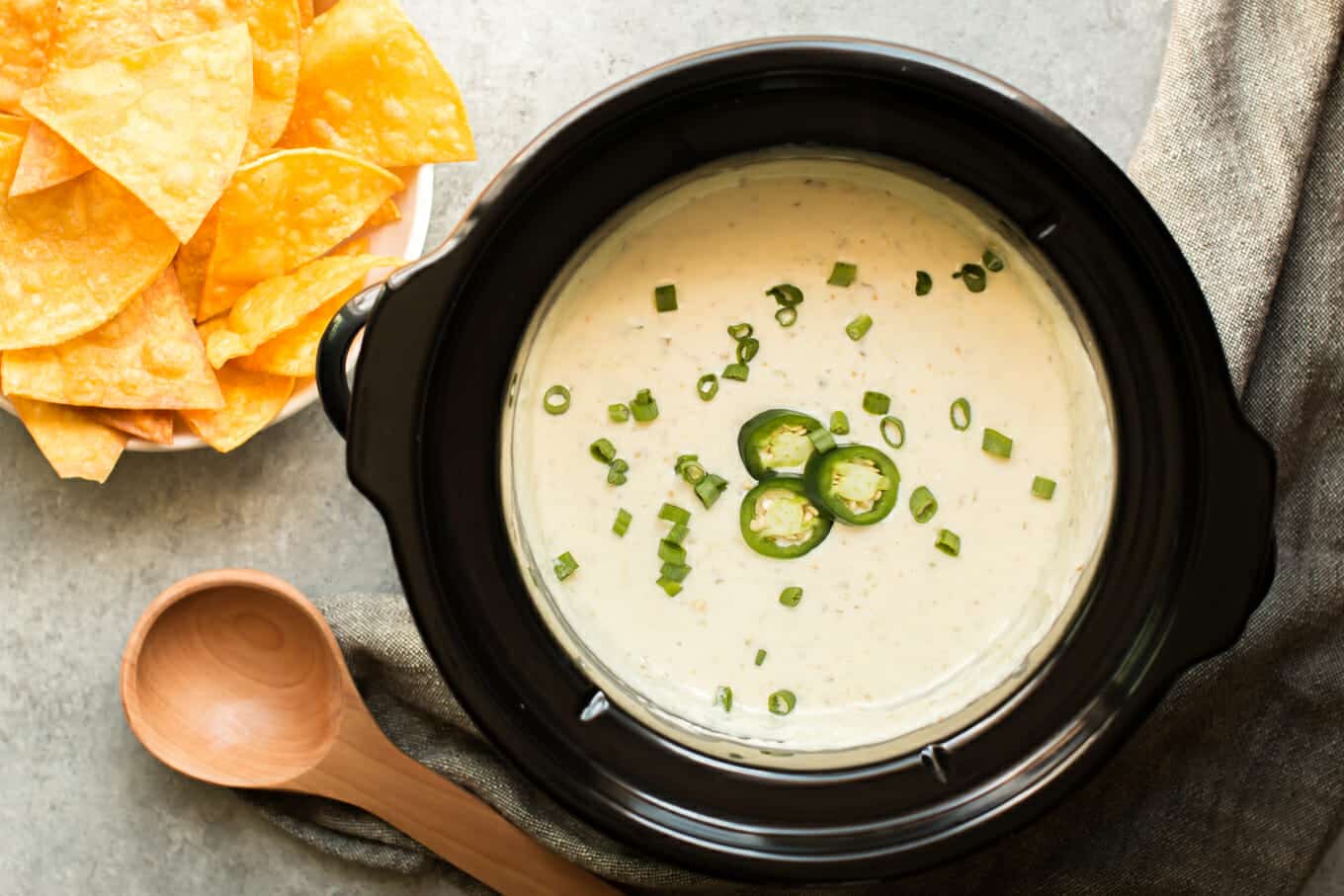 round slow cooker full of queso verde, chips on the side.