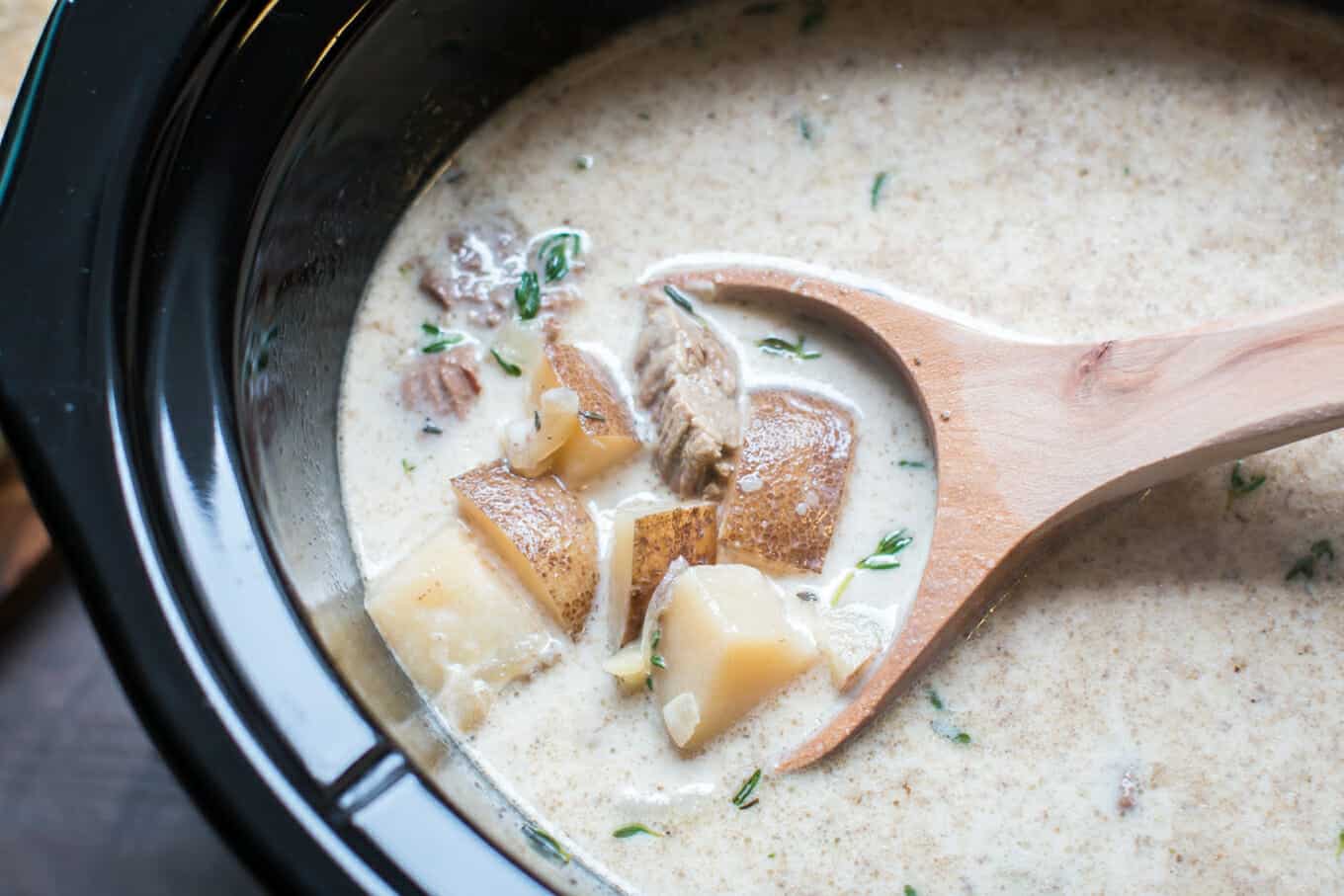 close up of steak and potato soup in slow cooker with thyme on top.