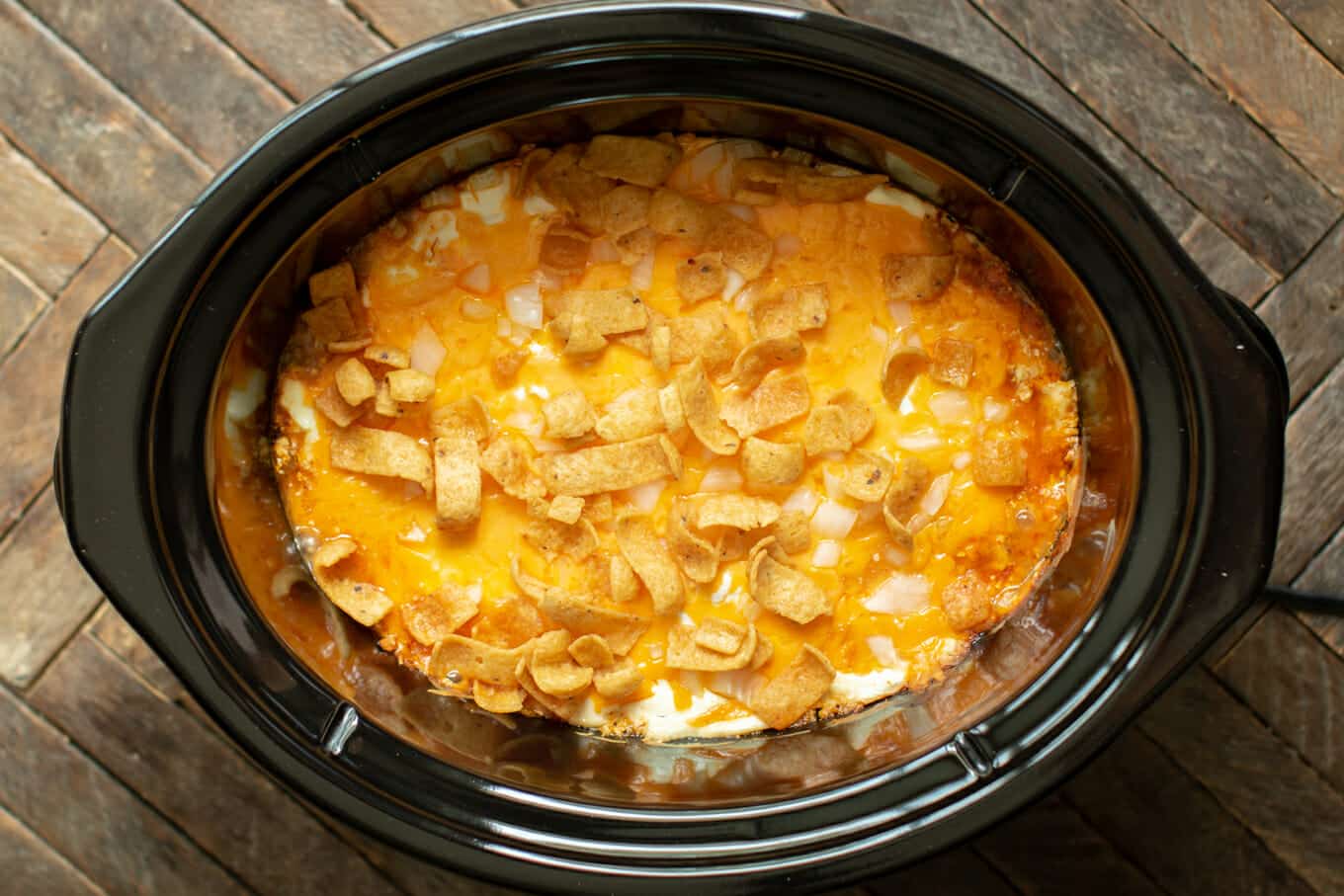 chili, sour cream, cheese, onion and fritos done cooking in a slow cooker.