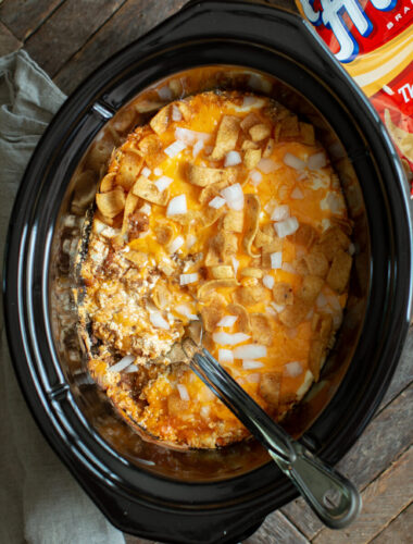 chili casserole with fritos and onion on top. Metal spoon in it.