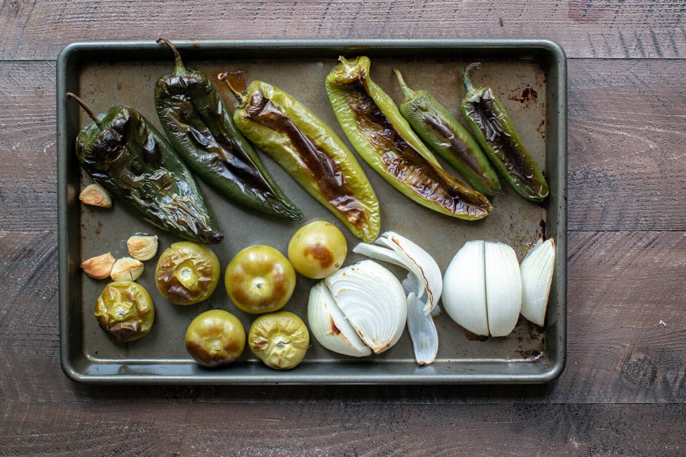 charred chiles, tomatillos, onion and garlic on a sheet pan.