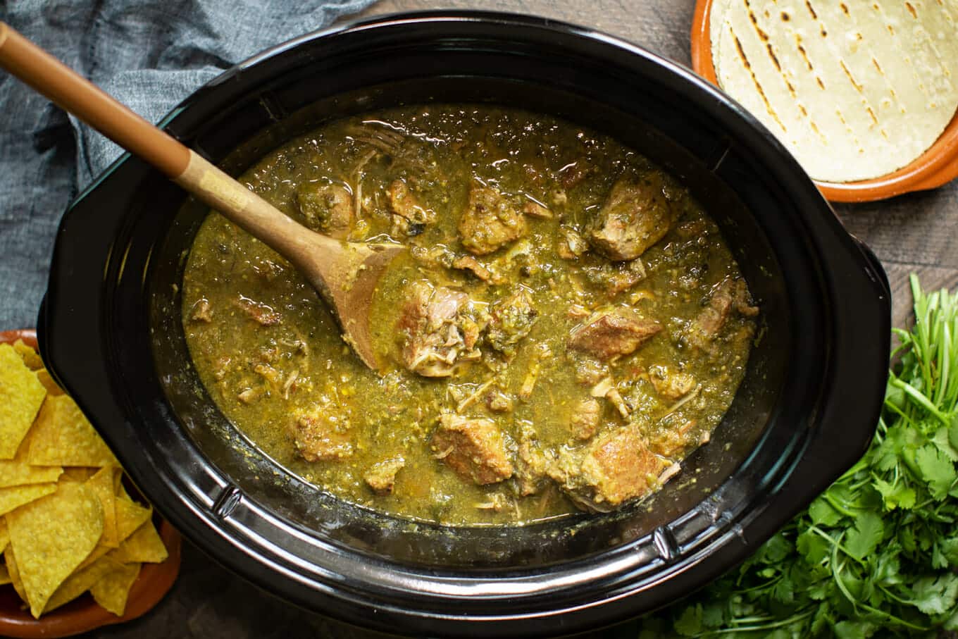 Finished cooking chile verde in the slow cooker with tortillas and cilantro on the side.