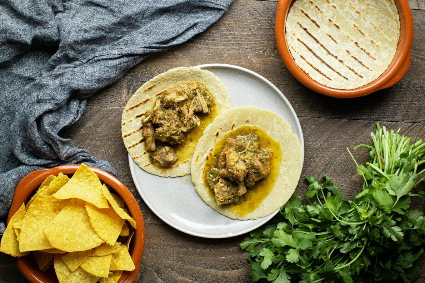 2 tortillas on a plate with pork chile verde on them.