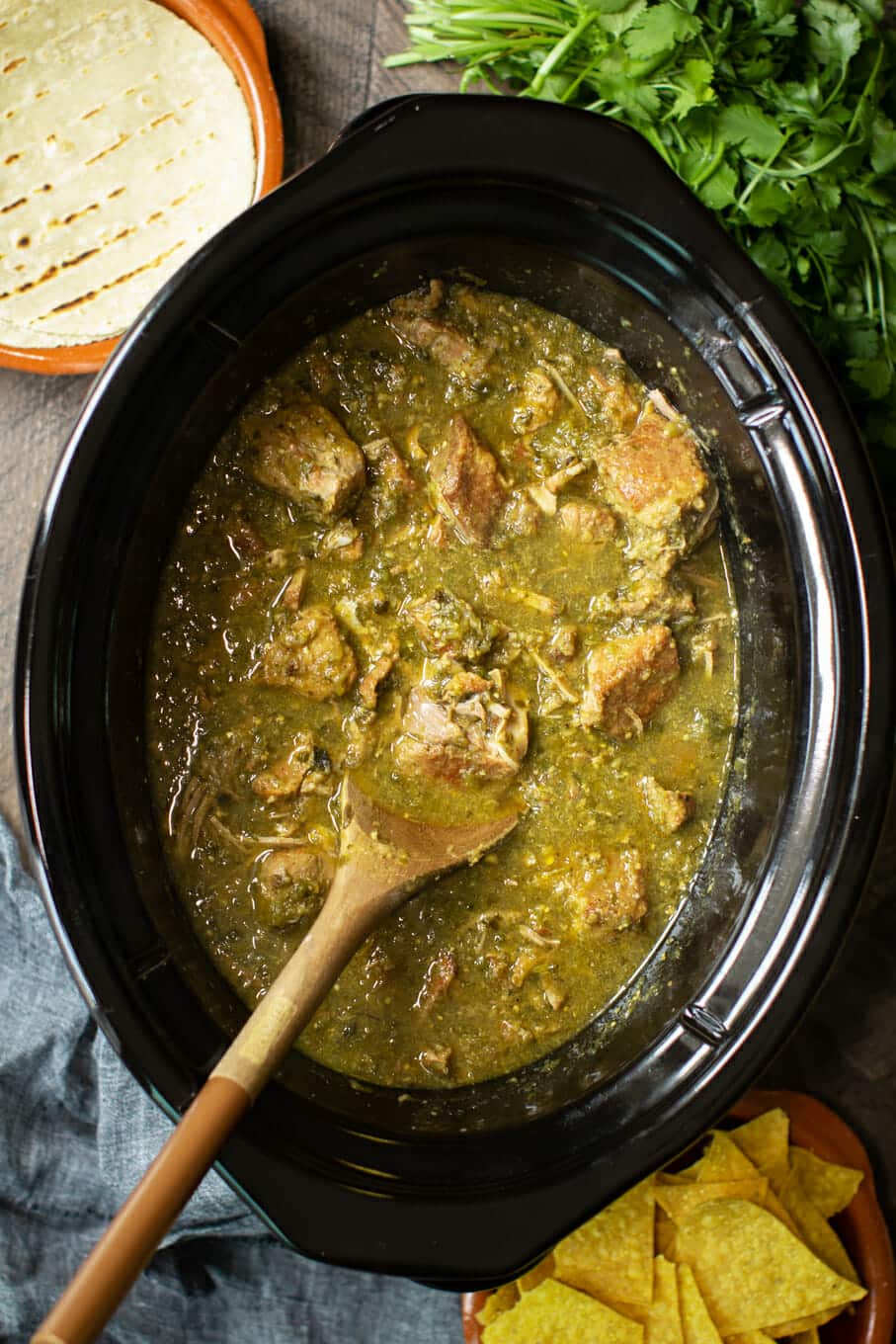 pork chile verde in slow cooker with wooden spoon in it.