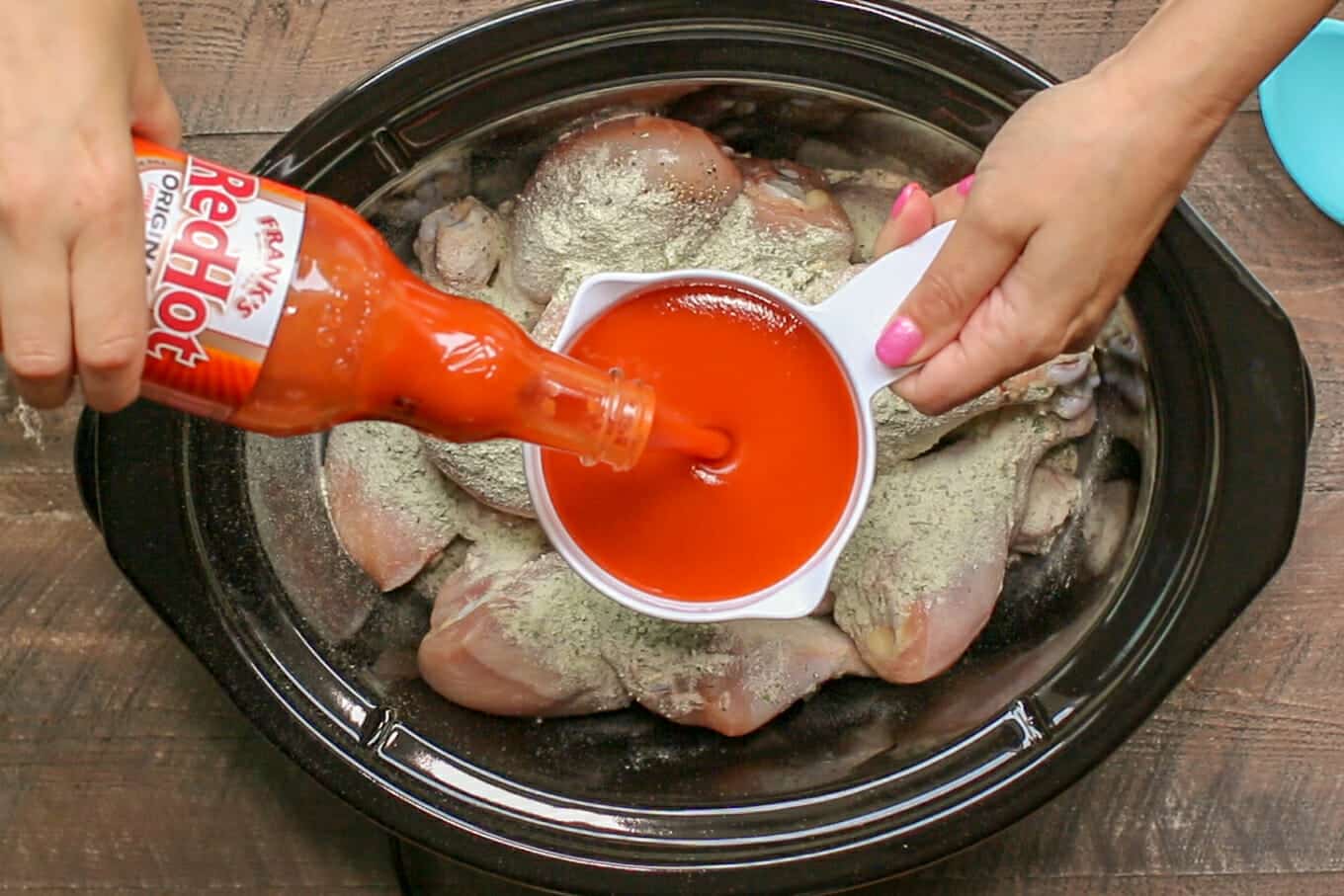 buffalo sauce being pour into a measuring cup over drumsticks in the slow cooker
