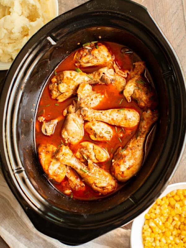 cooked drumsticks in a slow cooker in buffalo sauce with chives on top.