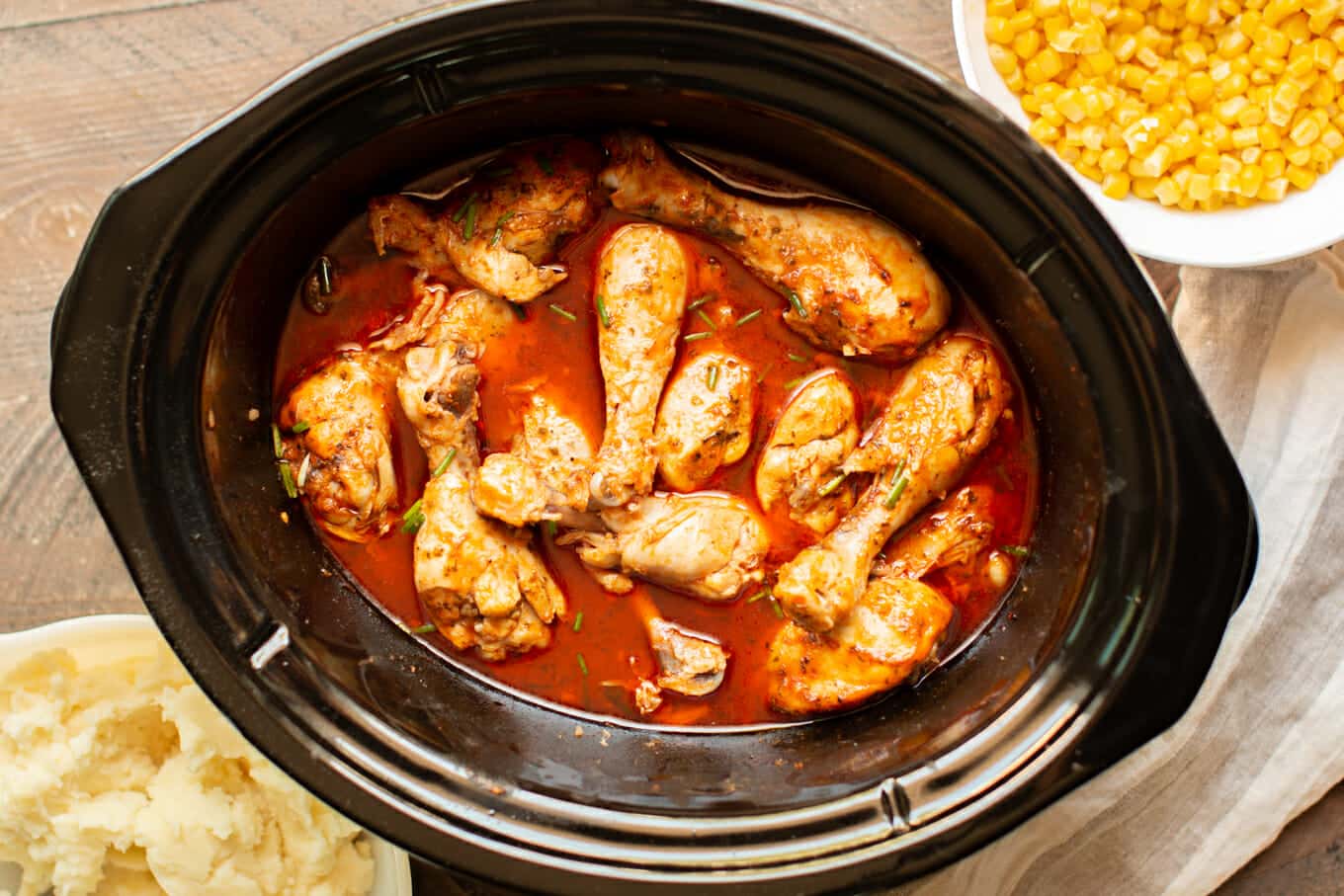 cooked drumsticks in a slow cooker with corn and mashed potatoes on the side.