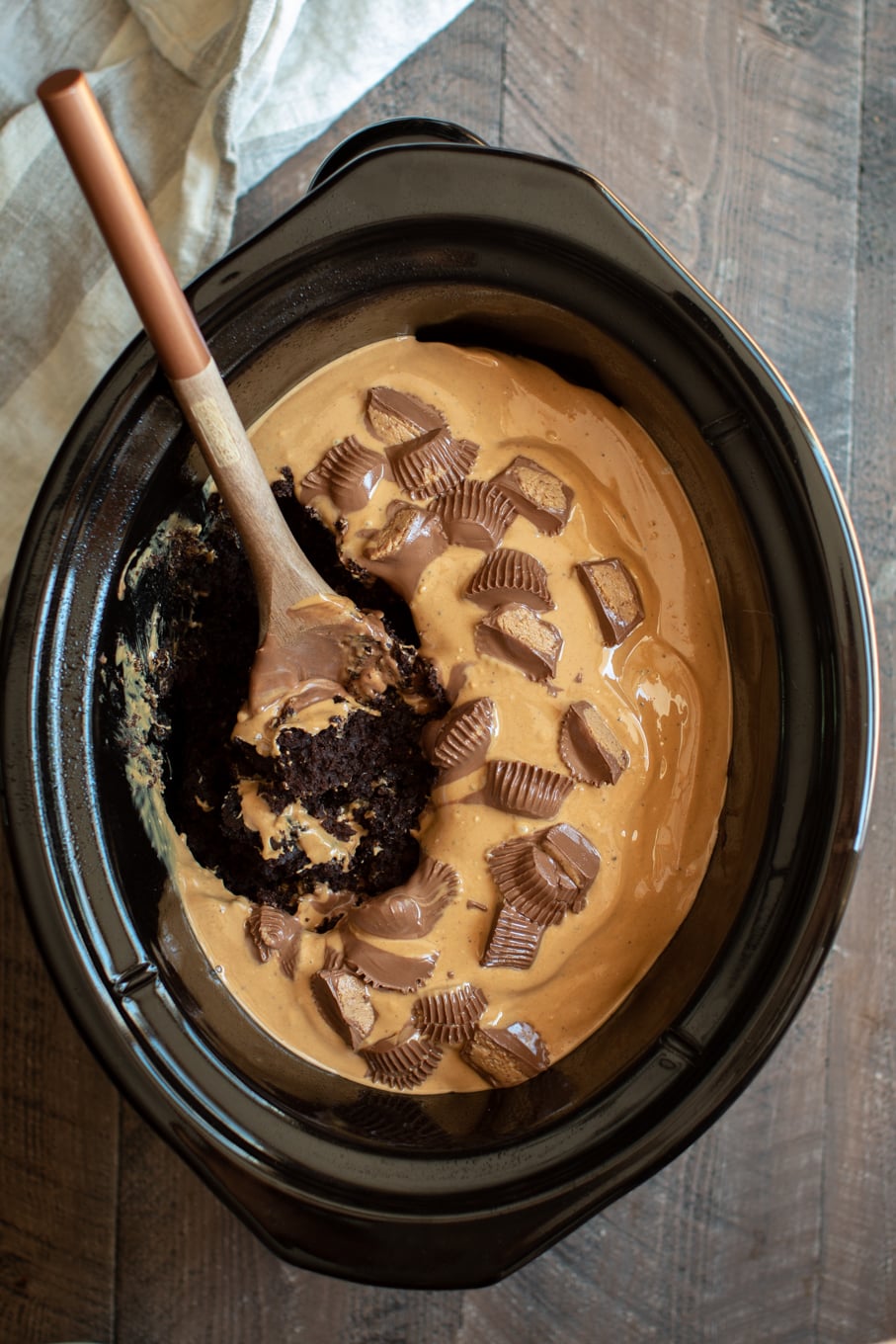 chocolate cake in slow cooker with peanut butter icing, wooden spoon in it.