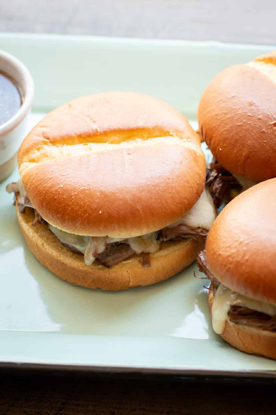 3 french dip sandwiches on teal platter.