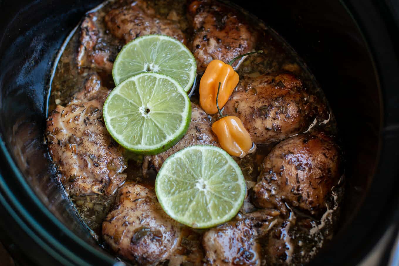 close up of Jamaican jerk chicken in slow cooker with limes and habaneros on top
