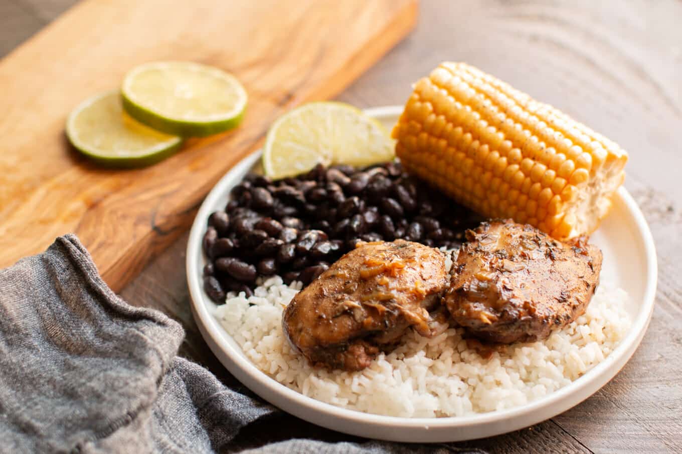 2 chicken thighs on rice with black beans and corm on white plate.