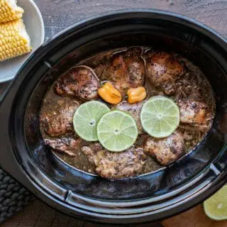 Jamaican jerk chicken in a slow cooker with limes and habanero on top.