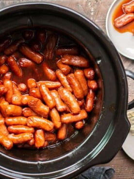 round slow cooker with little smokie wieners in it. Barbecue based sauce.
