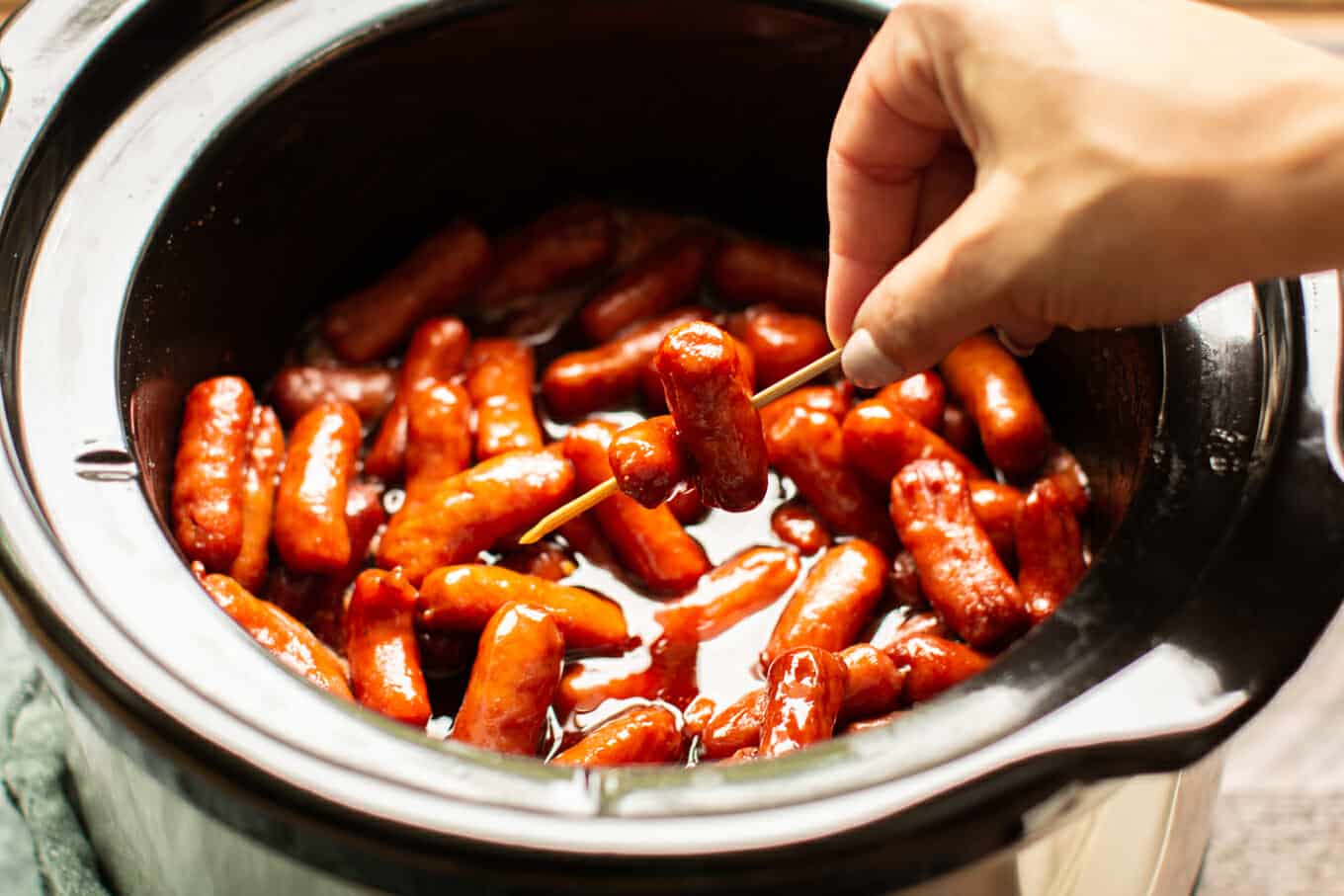 2 little smokie wieners on a toothpick, slow cooker in the background.