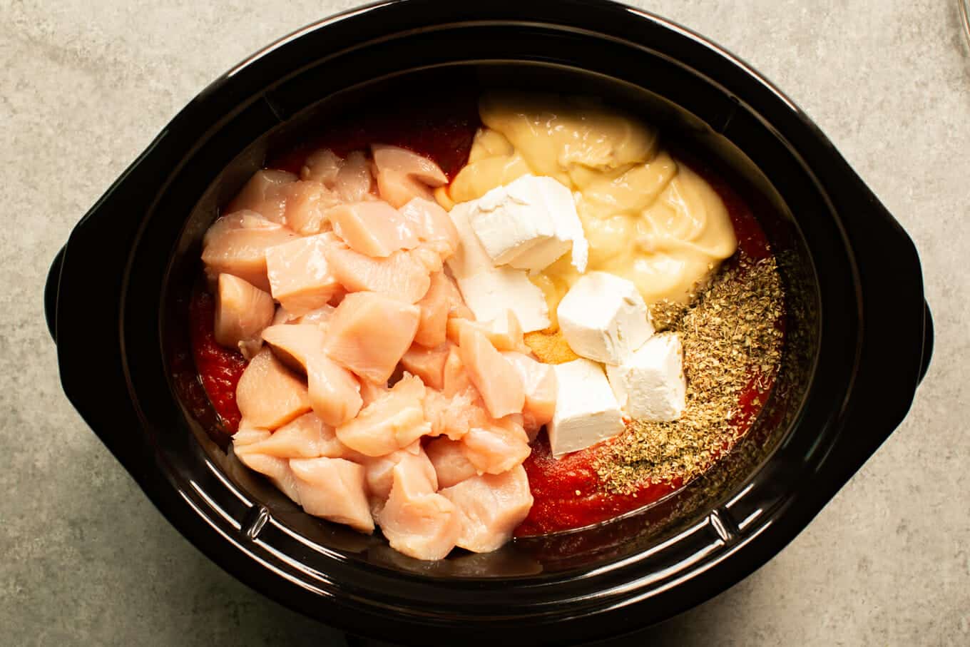 raw chicken cubes, cream cheese, cream of chicken, spices and marinara sauce in a slow cooker.