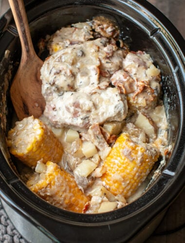 cooked pork chops, corn cobs, potatoes with spatula in slow cooker.