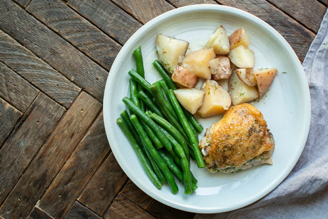 chicken thigh, potatoes, and green beans on plate.