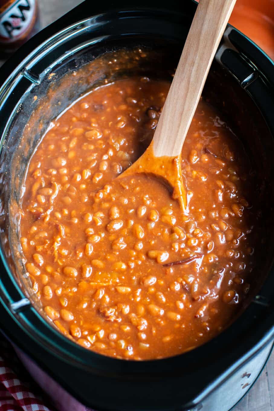 close up of root beer baked beans with wooden ladle in slow cooker