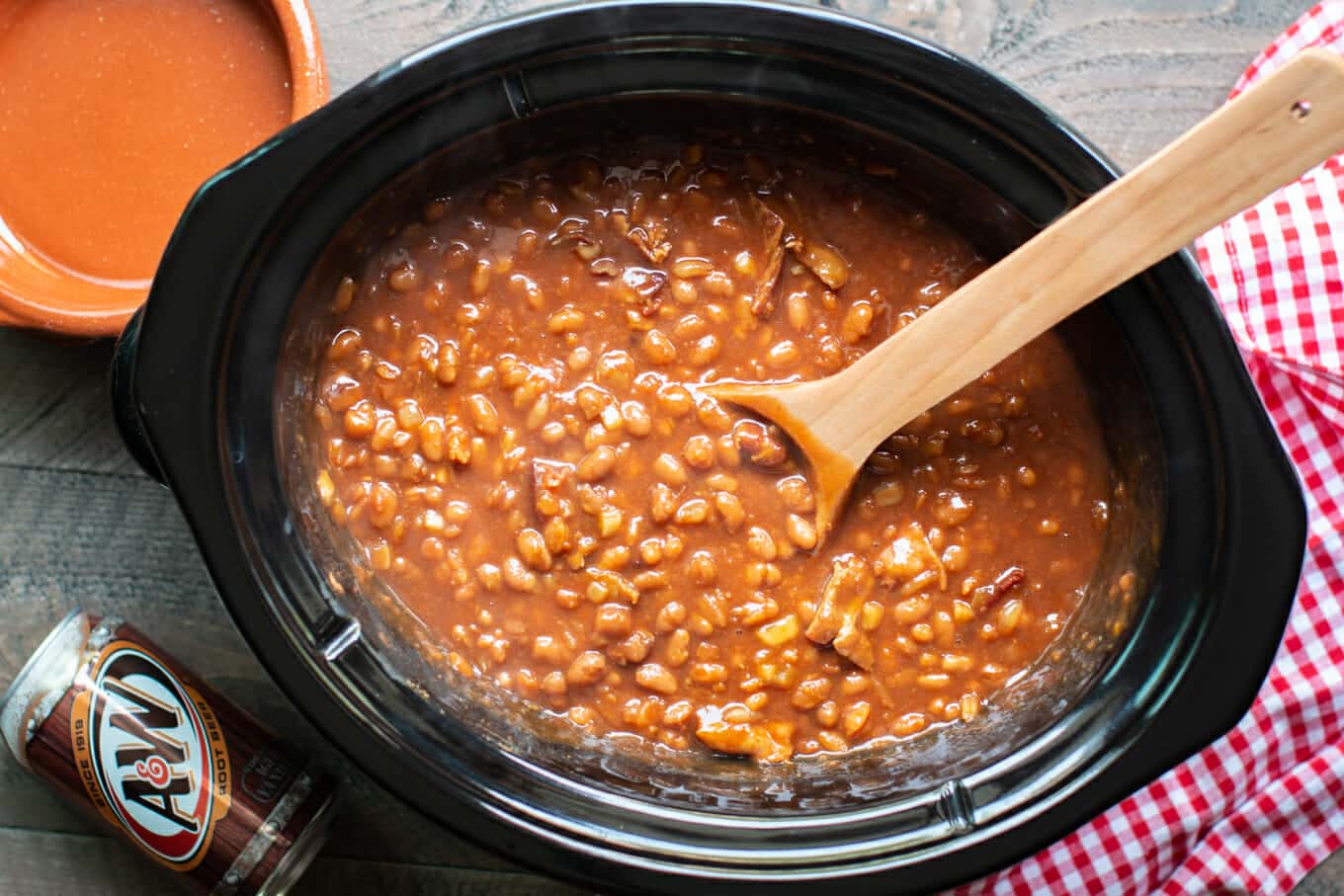 wooden spoon serving root beer beans from a slow cooker