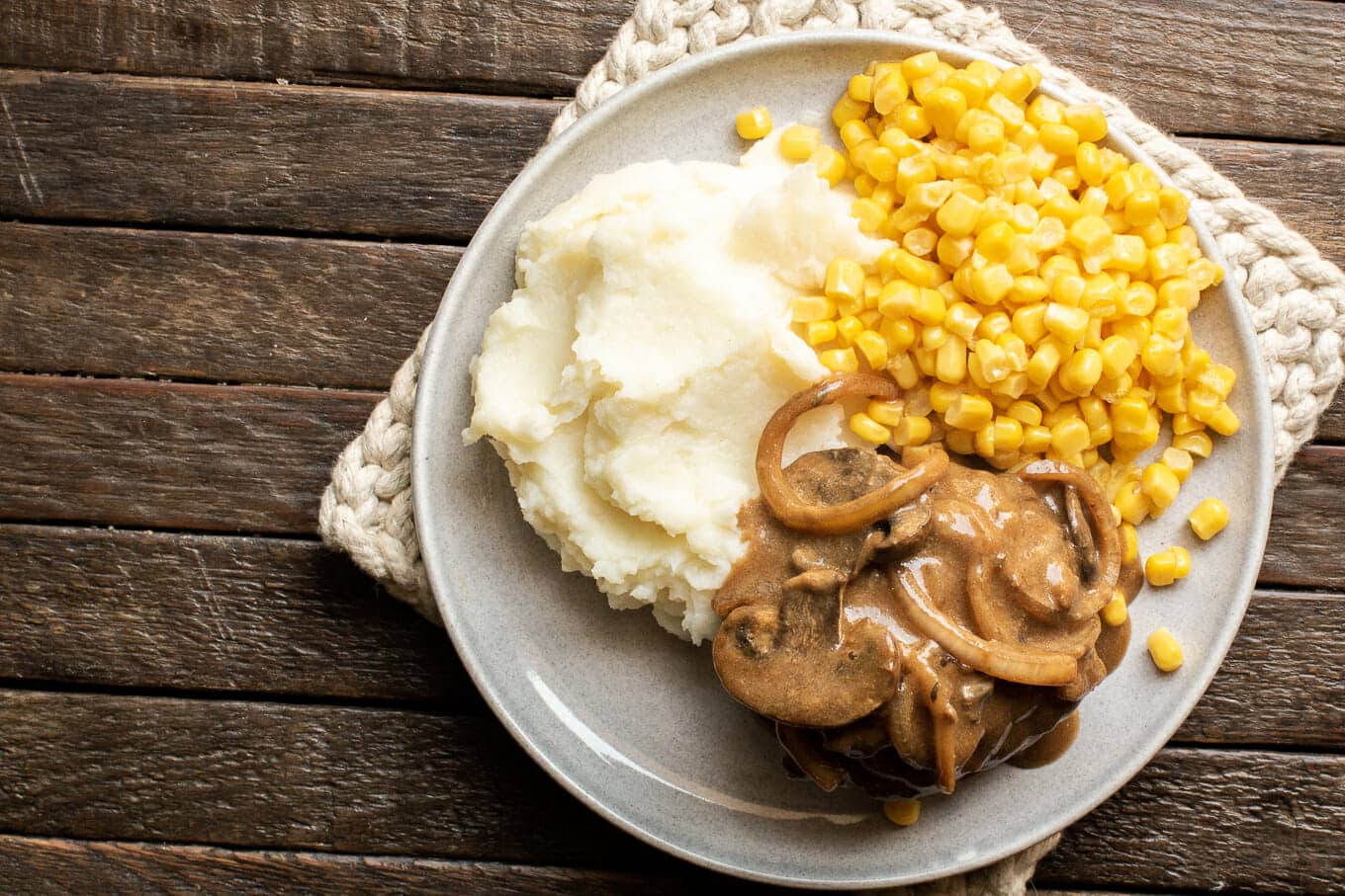 salisbury steak with gravy plated with corn and mashed potatoes