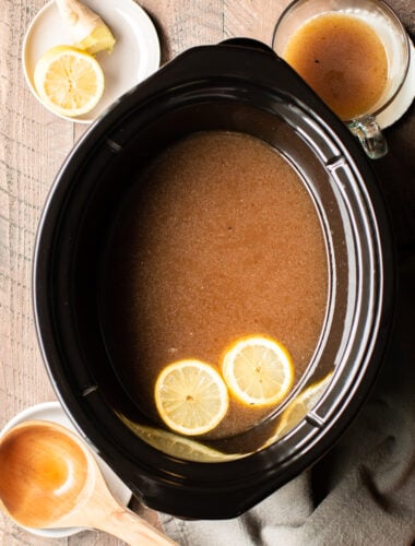 beef bone broth in the slow cooker with 2 lemon slices floating on top.