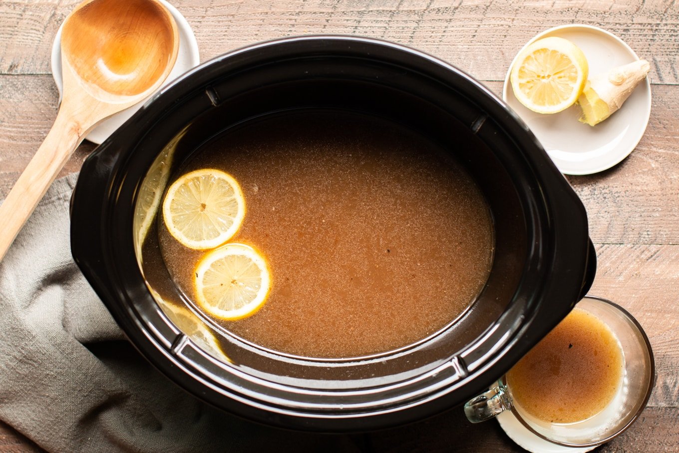 beef bone broth in slow cooker with lemons on side and bowl of bone broth on side.