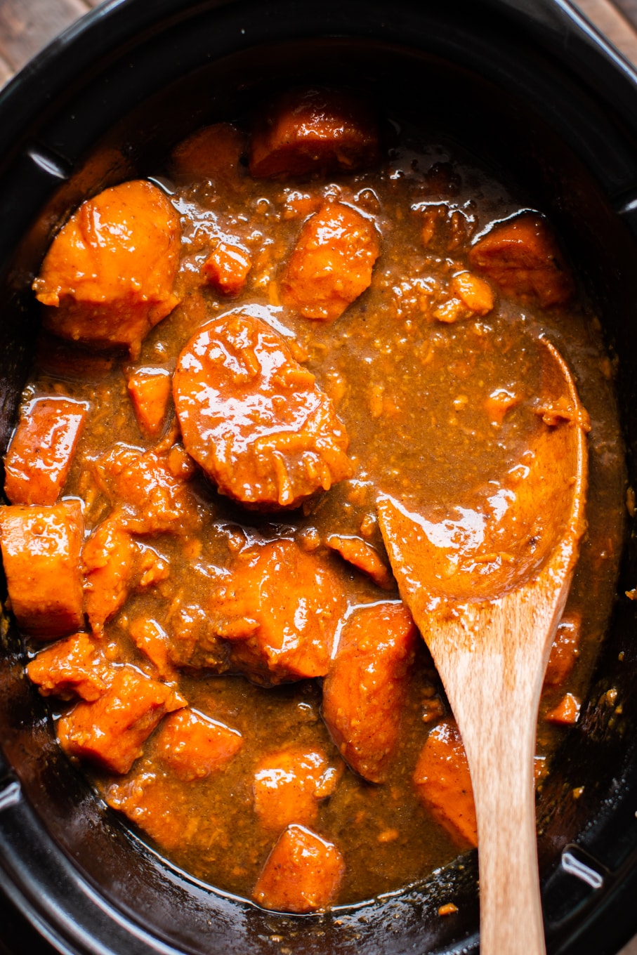 cooked yams in the slow cooker with wooden spoon in them.