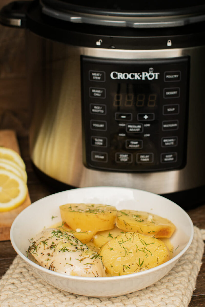 bowl of lemon chicken and potatoes in front of a pressure cooker.