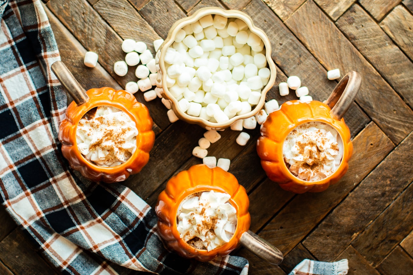 3 pumpkin mugs with whipped cream and nutmeg on top.