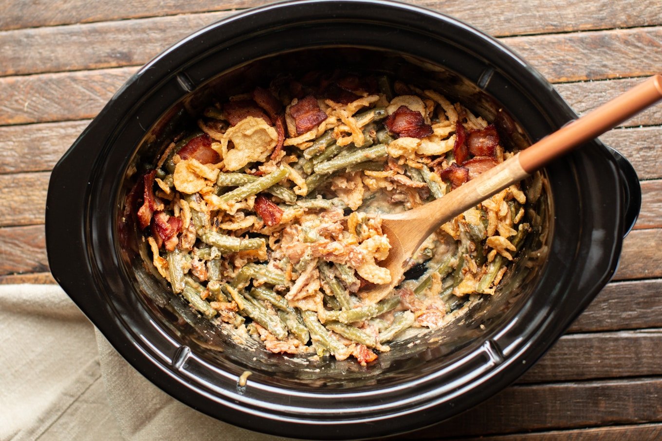 wooden spoon serving green beans from a slow cooker with french fried onions on top