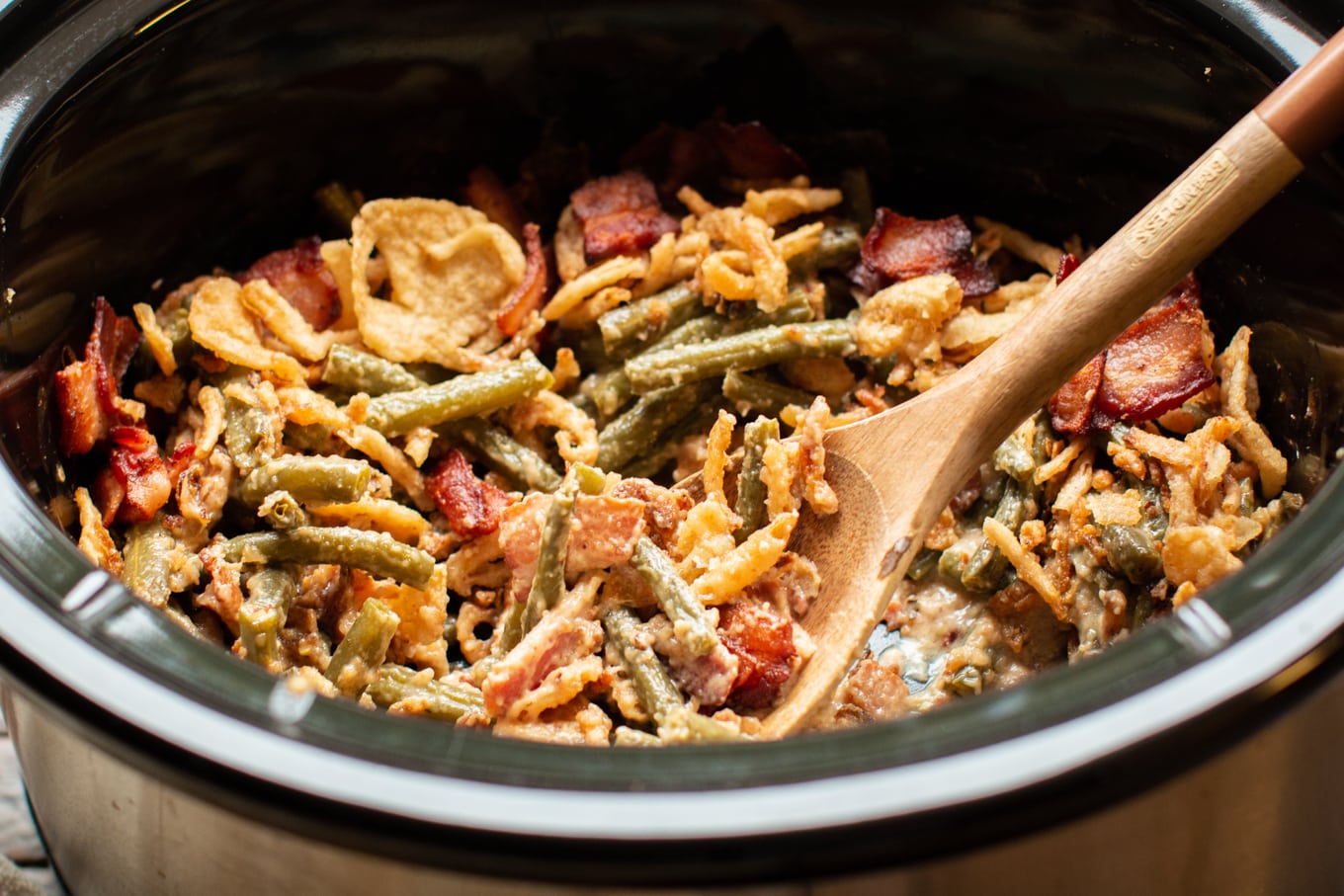 close up of green bean casserole with wooden spoon in it.