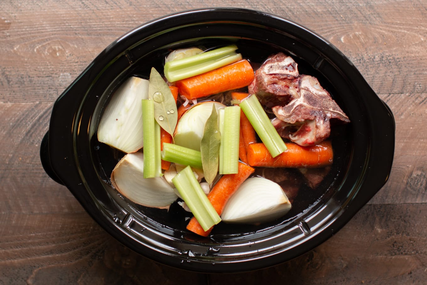 browned beef bones, onion, carrots, celery, onions and bay leaves in a slow cooker.