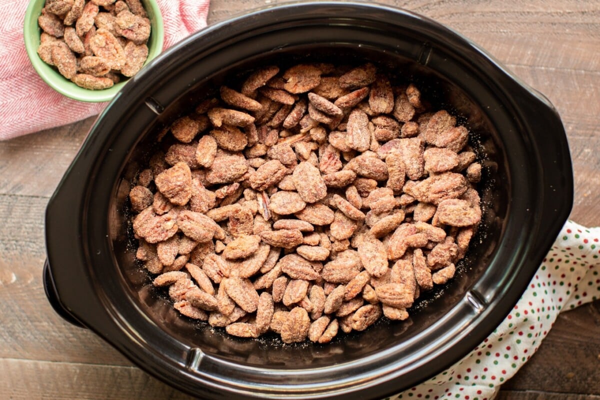 full slow cooker of cooked candied pecans with polka dot napkin on the side.