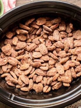 full slow cooker of cooked candied pecans with polka dot napkin on the side.