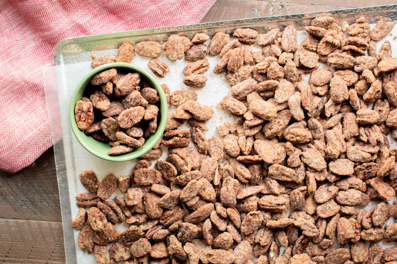 pecans on a wax paper-lined sheet tray. Some pecans in a small green bowl.