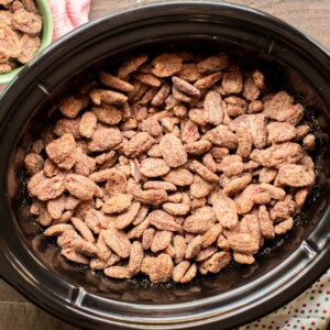 full slow cooker of cooked candied pecans with polka dot napkin on the side.