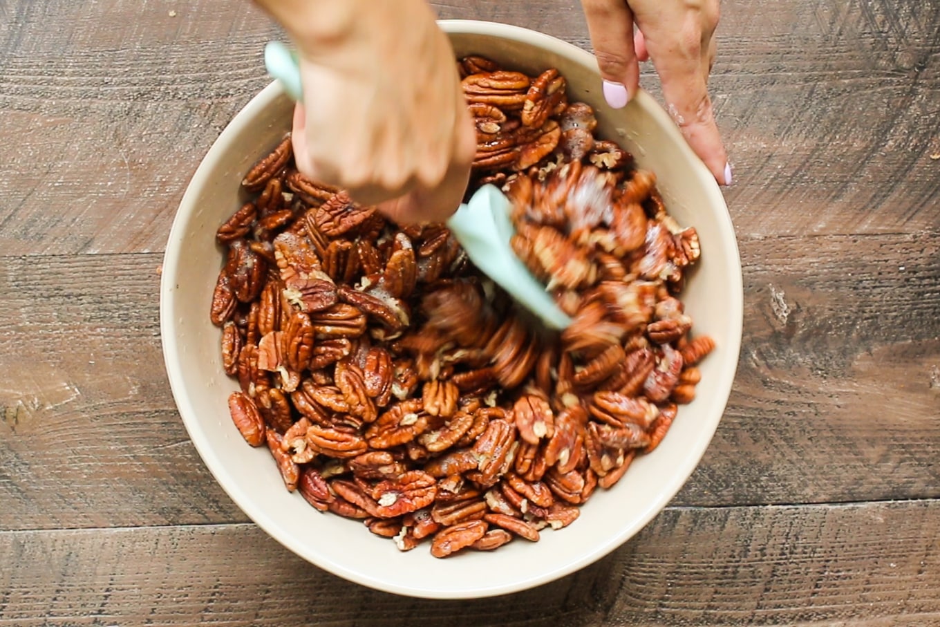 pecans being stirred with a green spatula.