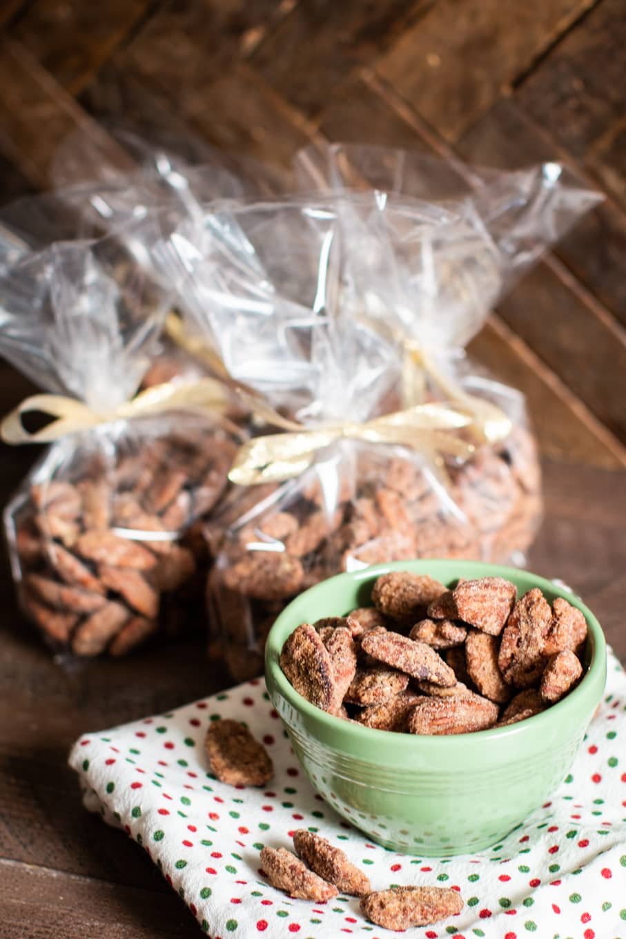 pecans in green bowl with more pecans in decorative bags in the background.