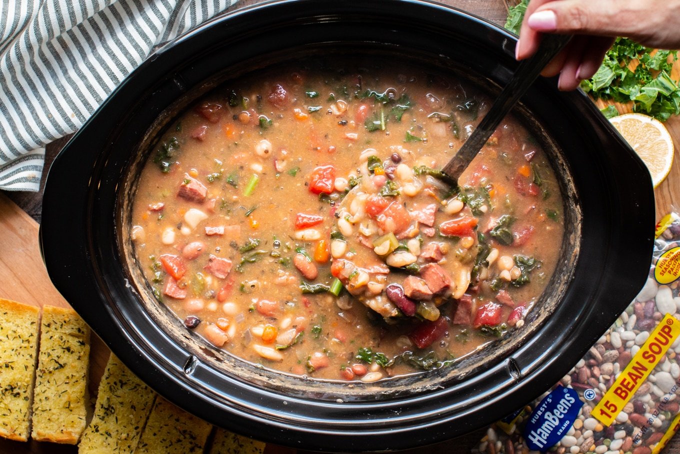 cooked 15 bean soup in slow cooker, ladle full of soup coming from slow cooker.