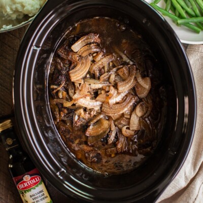 beef roast with balsamic sauce and onion in a slow cooker.