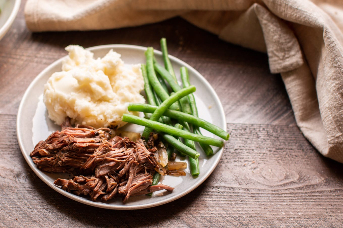shredded beef on gray plate with green beans and mashed potatoes.