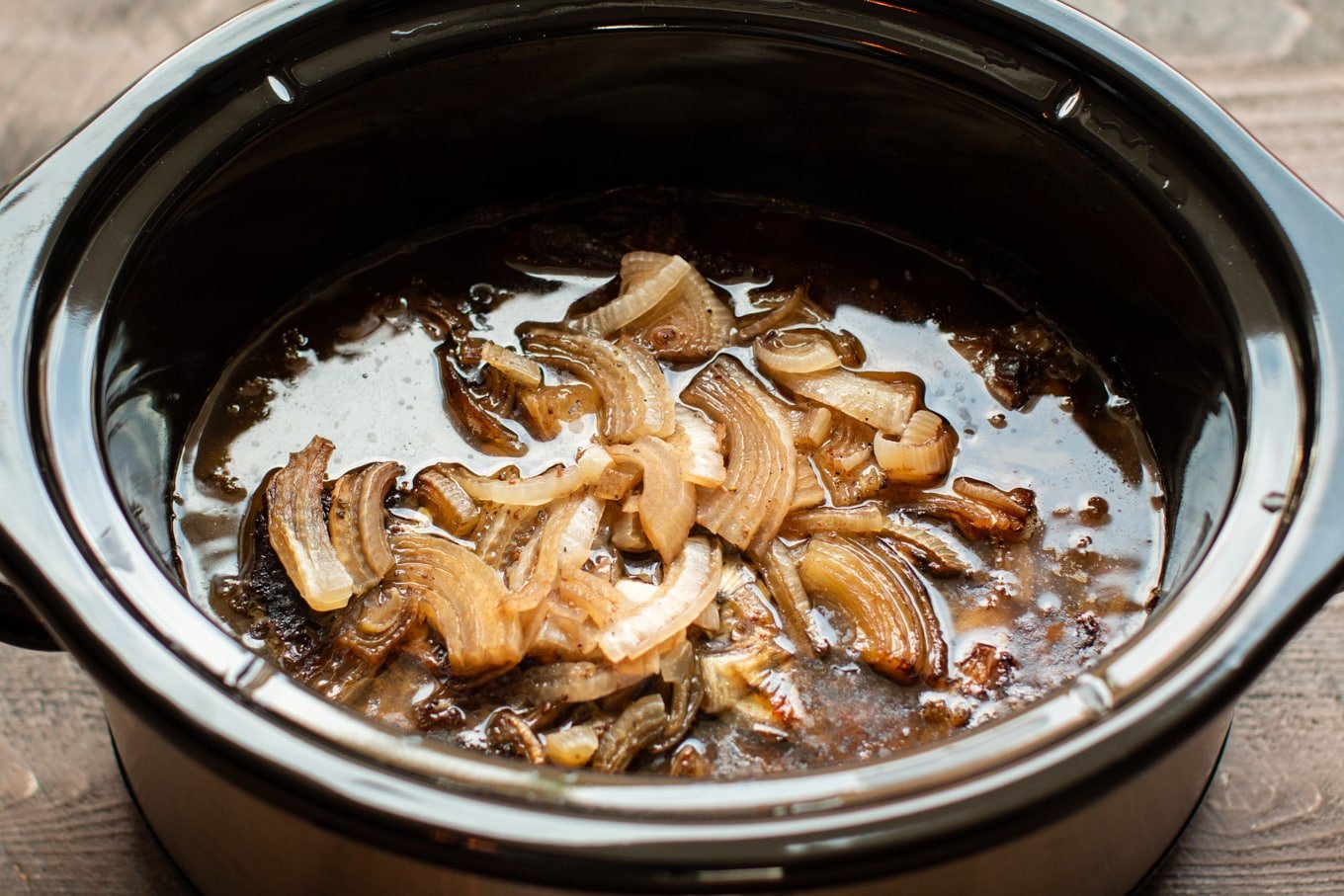 close up of balsamic beef roast with onions on top in slow cooker.