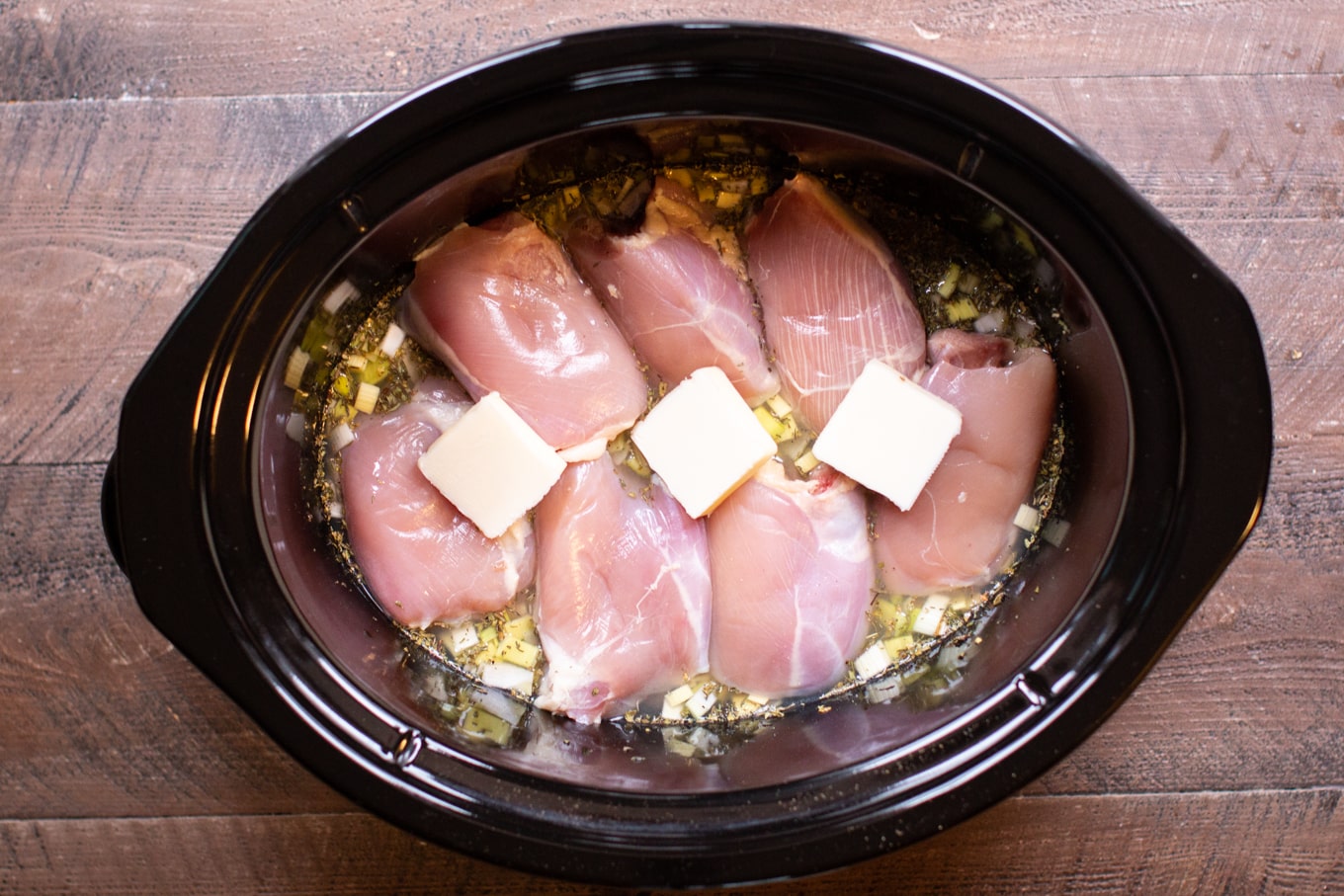 uncooked chicken thighs with pats of butter on top.