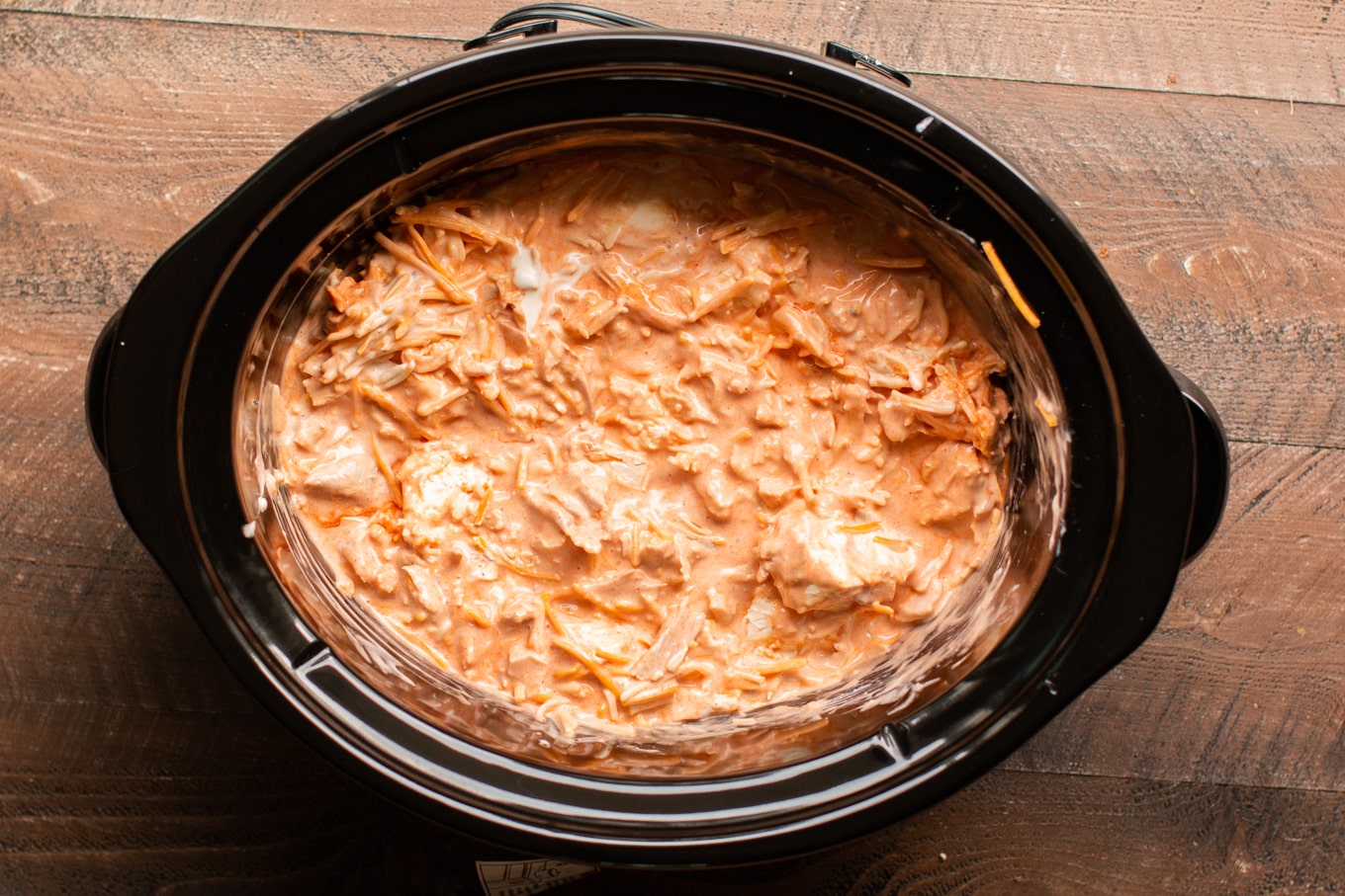 A mixture of buffalo chicken dip ingredients in the slow cooker, uncooked.